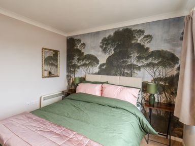 A bedroom with a bed green and pink bedding bedside tables green lamps and tree mural at Handale Banks Farm Lodge in Liverton