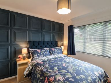 A bedroom with a floral bedspread dark paneled wall bedside tables lamps and a window with blinds at Handale Banks Farm Lodge Liverton