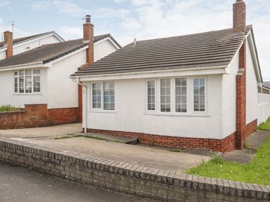 A bungalow with a paved driveway and a low brick wall at 31 Sisial Y Mor in Rhosneigr