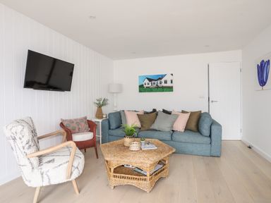 A living room with a blue sofa multiple cushions a wall-mounted TV and a wicker coffee table at 31 Sisial Y Mor in Rhosneigr