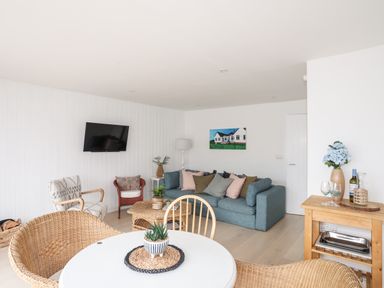 A living room with a sofa cushions chairs a round table and a wooden side table with flowers at 31 Sisial Y Mor in Rhosneigr