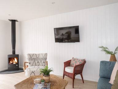 A living room with a wood burning stove two different chairs a wicker coffee table with plants and a wall mounted television at 31 Sisial Y Mor in Rhosneigr