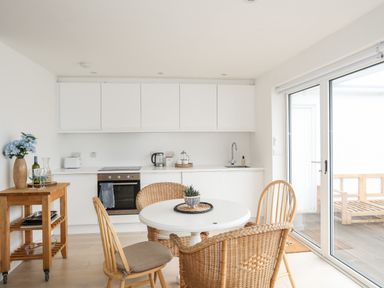 A kitchen with white cabinets a round table with chairs and a wooden side table at 31 Sisial Y Mor in Rhosneigr