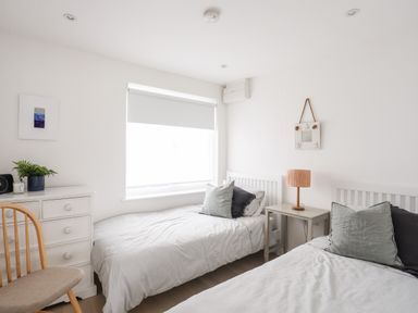 A bedroom with two single beds a small side table with a lamp a chair and a chest of drawers at 31 Sisial Y Mor in Rhosneigr
