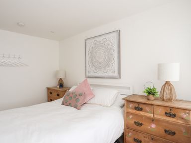 A bedroom with a bed white bedding two wooden bedside tables lamps and a decorative wall hanging at 31 Sisial Y Mor in Rhosneigr