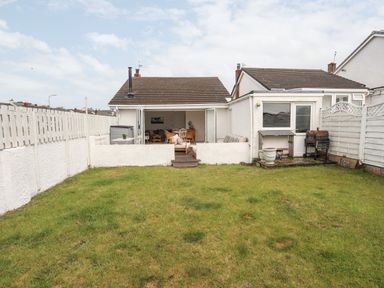 A backyard with a grass lawn a patio with outdoor furniture and a barbecue grill at 31 Sisial Y Mor in Rhosneigr