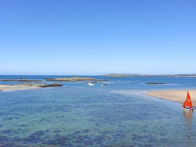 A coastal scene with several small boats on the water near a sandy shore at 31 Sisial Y Mor in Rhosneigr