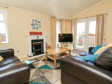 A living room with leather sofas a wooden coffee table a TV on a glass stand a fireplace and patio doors at Mojo Mullacott near Ilfracombe