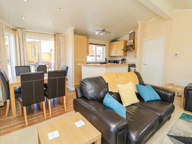 A living room with a black leather sofa and blue and yellow cushions near a wooden dining table with six chairs at Mojo Mullacott near Ilfracombe