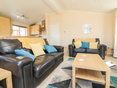 A living room with black leather sofas with cushions a wooden coffee table and kitchen cabinets in the background at Mojo in Mullacott near Ilfracombe