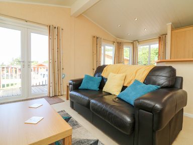 A living room with a black leather sofa and colored cushions near a wooden coffee table and windows at Mojo Mullacott near Ilfracombe