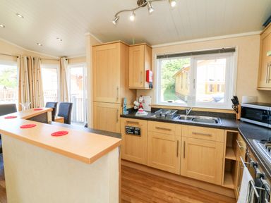 A kitchen with wooden cabinets a double sink microwave and dining table with chairs at Mojo Mullacott near Ilfracombe