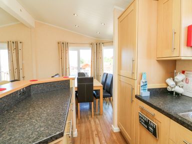 A kitchen with wooden cabinets and black countertops looking into a dining area with a wooden table and black chairs at Mojo Mullacott near Ilfracombe
