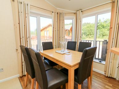 A dining area with a wooden table and six black chairs surrounded by windows at Mojo Mullacott near Ilfracombe