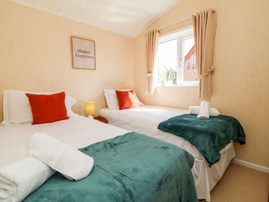 A bedroom with two single beds with white sheets red pillows teal throws and rolled towels at Mojo in Mullacott near Ilfracombe