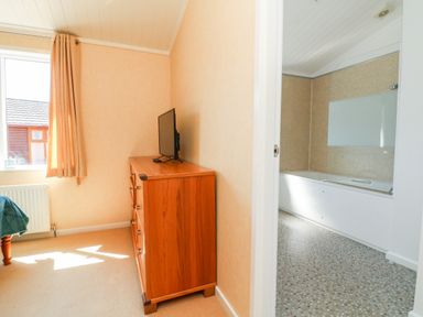 A bedroom with a wooden dresser and a television next to a window and an adjoining bathroom with a bathtub at Mojo in Mullacott near Ilfracombe
