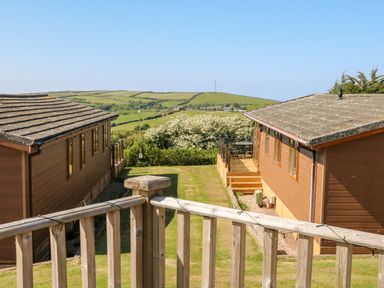 Two wooden cabins with grassy area between them and countryside view at Mojo in Mullacott near Ilfracombe
