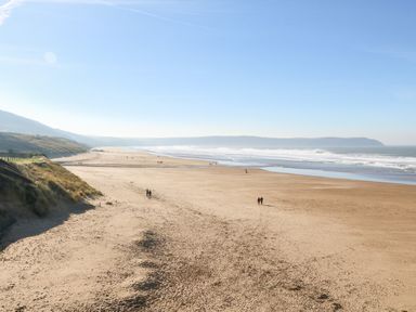 A wide sandy beach with a few people walking and ocean waves at Mojo Mullacott near Ilfracombe
