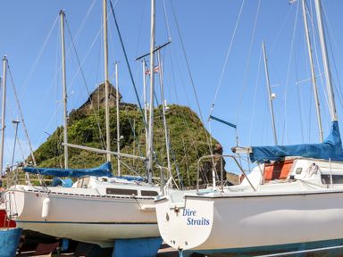 Sailboats docked in a marina with a grassy hill and stone building in the background at Mojo Mullacott near Ilfracombe