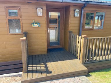 A wooden porch with a glass door and railings on a brown building at Mojo in Mullacott near Ilfracombe