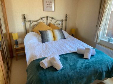 A bedroom with a bed with pillows and rolled towels beside a window at Mojo in Mullacott near Ilfracombe