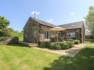 A stone house with a patio umbrella and outdoor seating in a garden at Traeth Ora in Moelfre
