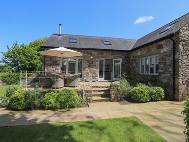 A stone house with a patio table and umbrella outside with garden at Traeth Ora in Moelfre