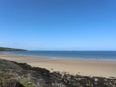 A beach with sand and rocks by the sea under a clear sky at Traeth Ora in Moelfre