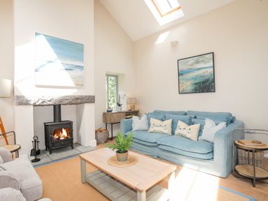 A living room with a blue sofa a light wood coffee table a wood burning stove and paintings on the walls at Traeth Ora in Moelfre