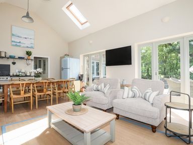 A living room with two armchairs and a coffee table next to a dining table and kitchen area at Traeth Ora in Moelfre