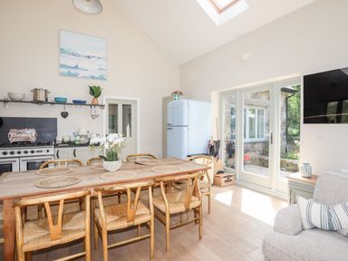 A kitchen dining area with a wooden table and chairs a blue fridge a stove and glass doors leading outside at Traeth Ora in Moelfre