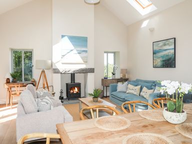 A living room with sofas a wood burning stove coffee table and dining table at Traeth Ora in Moelfre