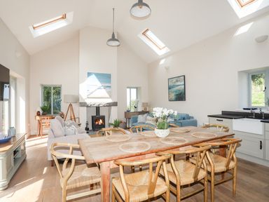 A dining table with six chairs and a vase of flowers next to a living area with sofas and a fireplace at Traeth Ora in Moelfre