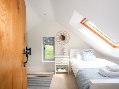 A bedroom with a single bed a bedside table with a lamp a small window with a sailboat curtain and a skylight window at Traeth Ora in Moelfre