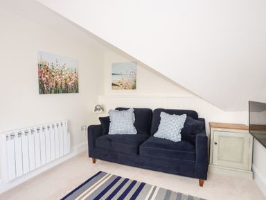 A small living area with a dark blue sofa with checkered cushions next to a small cabinet and paintings on the wall at Traeth Ora in Moelfre