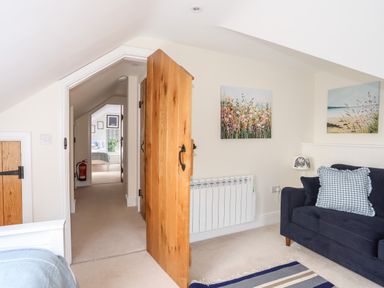 A hallway with open wooden doors leading to bedrooms with beds and wall art at Traeth Ora in Moelfre