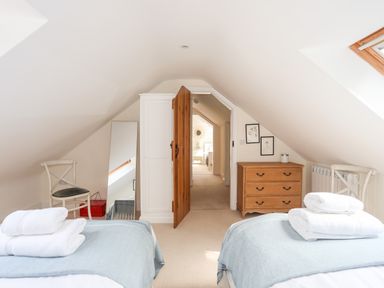A bedroom with two beds, chairs, a mirror, a wooden door, a dresser, and framed pictures at Traeth Ora in Moelfre