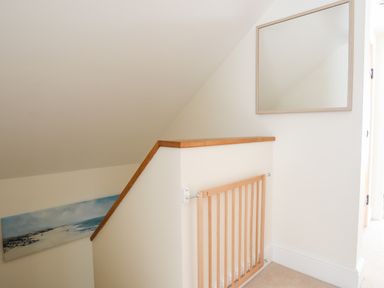 A staircase with a wooden safety gate and a mirror on the wall at Traeth Ora in Moelfre