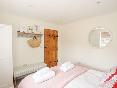A bedroom with a wooden door a bench beneath a shelf with framed pictures a round mirror and a bed with folded towels at Traeth Ora in Moelfre