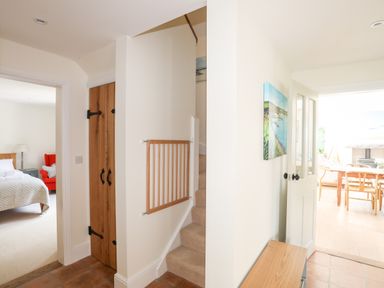 A hallway with stairs a wooden cupboard a baby gate a bedroom on the left and a dining area on the right at Traeth Ora in Moelfre
