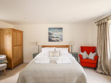 A bedroom with a bed two bedside tables lamps a wooden wardrobe and a red armchair at Traeth Ora in Moelfre