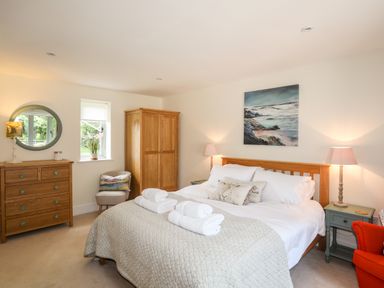 A bedroom with a large bed with folded towels on it wooden wardrobe wooden dresser with a round mirror and two bedside tables with lamps at Traeth Ora in Moelfre