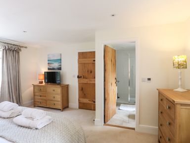 A bedroom with a bed covered with folded towels two wooden dressers a lamp a television and an open door leading to a bathroom at Traeth Ora in Moelfre