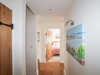 A hallway with terracotta tiled floor a wooden door partially open showing a bedroom and a painting on the wall at Traeth Ora in Moelfre