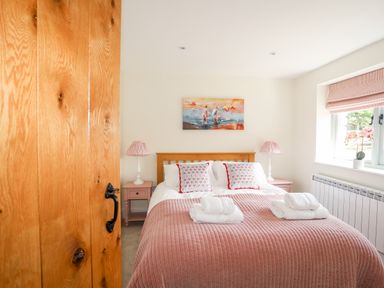 A bedroom with a wooden bed frame pink bedding two bedside tables with lamps a window with a blind and a painting on the wall at Traeth Ora in Moelfre