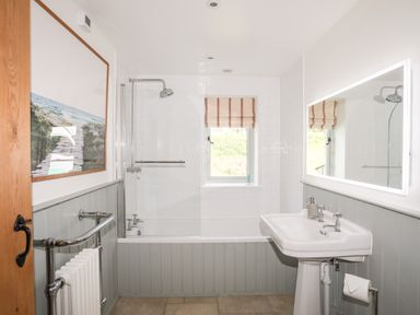 A bathroom with a bathtub shower sink mirror window and radiator at Traeth Ora in Moelfre