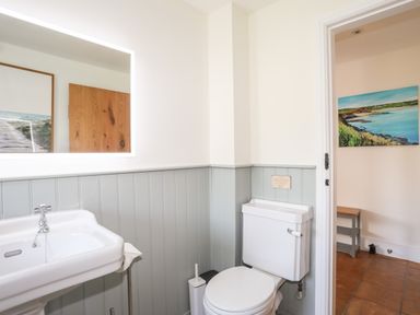 A bathroom with a white sink and toilet and a mirror showing another room with a painting at Traeth Ora in Moelfre