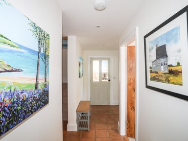 A hallway with tiles on the floor a bench by the wall and paintings hanging on each side at Traeth Ora in Moelfre
