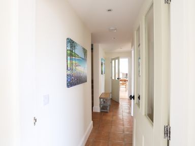 A hallway with tiled floor paintings on the wall a small bench and an open door leading to a dining area at Traeth Ora in Moelfre