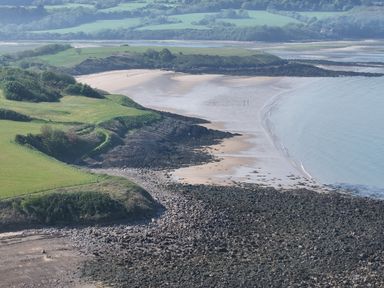 A coastline with a rocky shore grassy cliffs and sandy beach at Traeth Ora in Moelfre